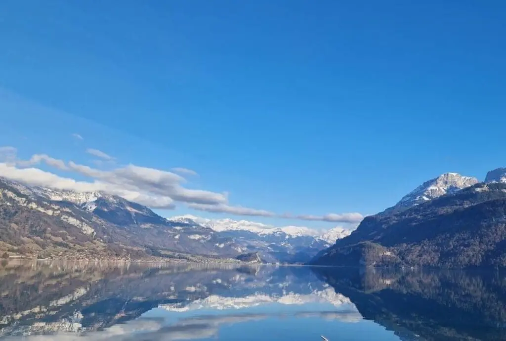 Die Berge und der Himmel spiegeln sich im Brienzersee. Der Himmel ist blau.