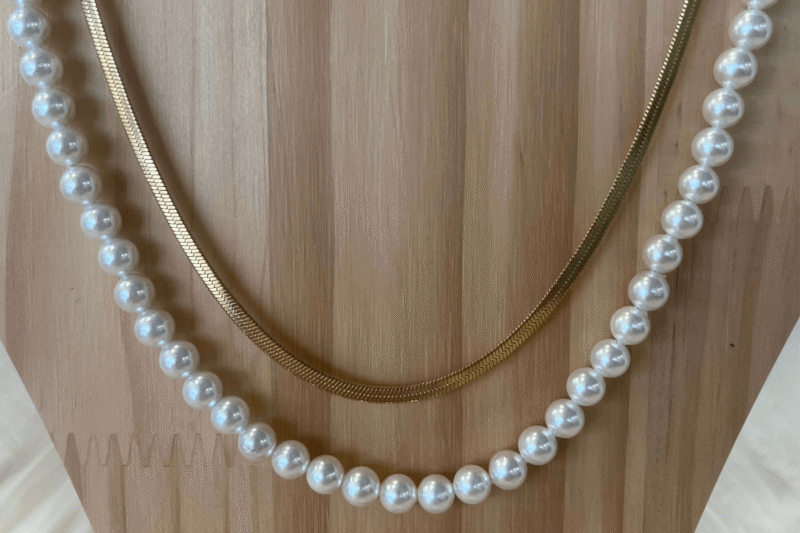 Auf dem Bild ist eine Holzbüste. Daran ist eine Perlenkette und eine vergoldete Kette.