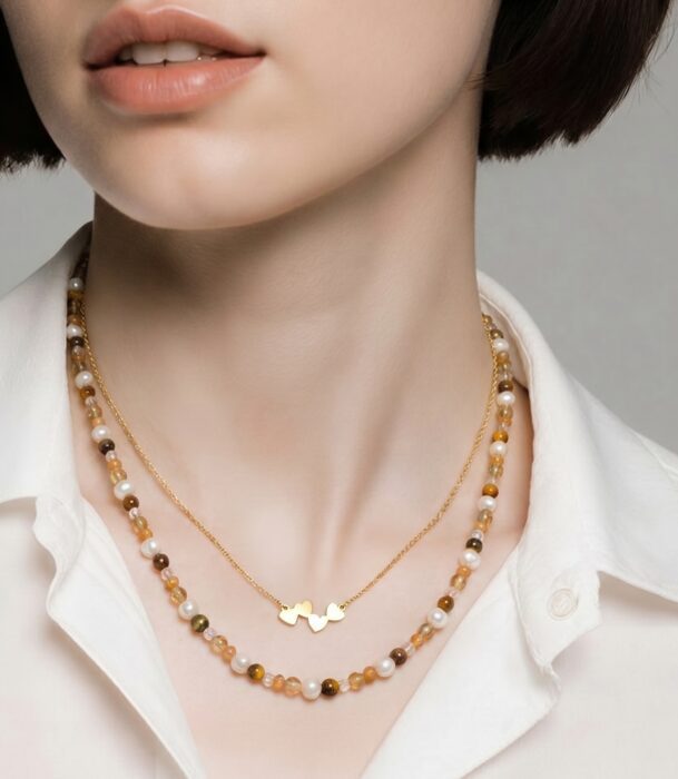 Minimalistisches Schmuck-Layering in warmen Naturtönen mit feiner Goldkette und modernem Editorial-Look.